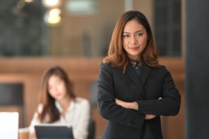 Confident female leader standing with arms crossed in a professional setting, representing the shift from inner critic to inner champion discussed in the article.